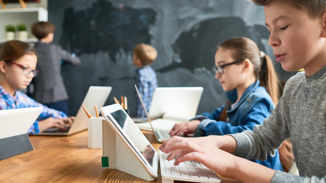 iStock.com/mediaphotos Kinder sitzen im Klassenzimmer vor dem Tablet