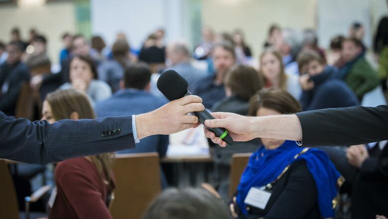 Foto: Kay Herschelmann Eine Person übergibt ein Mikrophone einer anderen Person